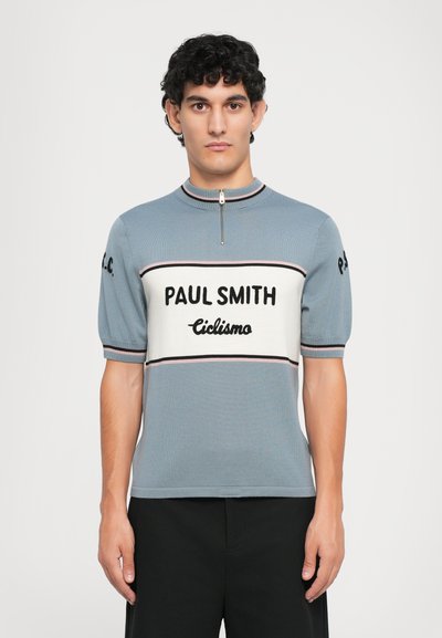 Pletená polo tričko s krátkým rukávem v světle modré barvě, vybavené zipovým výstřihem, výrazným logem "PAUL SMITH" a kontrastním pruhem s nápisem "Ciclismo" v černé barvě na hrudi.