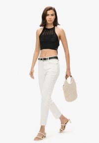 Top corto de punto negro, jeans rectos blancos, cinturón negro con hebilla plateada, bolso de mimbre beige y sandalias blancas de tacón bloque.