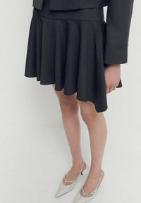 Black flared skirt made from soft fabric, featuring a smooth texture and an asymmetrical hem. Paired with light gray pointed shoes.