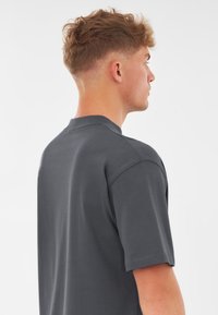 Szara bawełniana koszulka z krótkim rękawem, luźny krój i okrągły dekolt. Widoczne szwy na ramionach i rękawach.