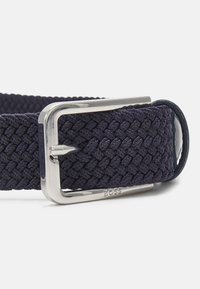 Ceinture tissée bleu marine avec une boucle en métal argenté. Présente une texture tressée et un détail de marque près de la boucle. Design durable et flexible.
