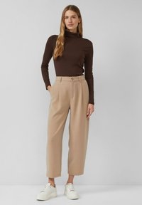Braunes Langarm-Top mit Rollkragen, kombiniert mit hoch taillierten beigen Hosen und weißen Sneakers, mit maßgeschneiderter Passform und seitlichen Taschen.