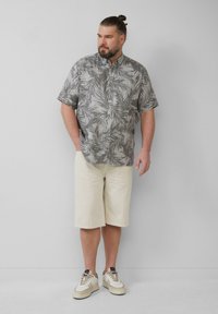Korte mouwen blouse met een grijs palmenbladpatroon, gecombineerd met crèmekleurige short en beige sneakers met donkere accenten.