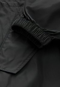 Tessuto in nylon nero con polsini elasticizzati arricciati, texture liscia e cuciture evidenti, caratterizzato da una finitura opaca e un design minimalista.