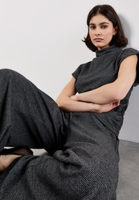 Grijze geruite jumpsuit met korte mouwen en een hoge hals. Losvallende pijpen met een zachte textuur, wat een ontspannen silhouet creëert.