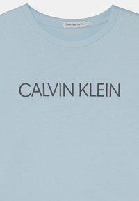 Hellblaues Baumwoll-T-Shirt mit rundem Halsausschnitt und dem Schriftzug "CALVIN KLEIN" in dunkelgrauem Druck über der Brust.