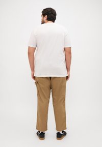 Hvid bomulds T-shirt med korte ærmer, parret med beige cargo-bukser med sidelommer, båret med sorte sneakers og en lys sål.