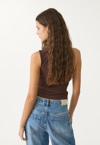 Top aderente marrone con scollatura rotonda, abbinato a jeans in denim blu a vita alta con etichetta e design della tasca classico.