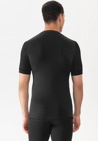 Zwart atletisch shirt met korte mouwen, een getailleerd ontwerp, gestructureerde mouwen en een gladde stof voor het lichaam. Naaidetails zichtbaar bij de zoom en de schouders.