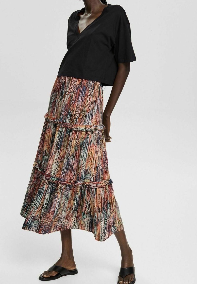 Haut noir à manches courtes associé à une jupe maxi multicolore à volants présentant un motif abstrait texturé. Des sandales noires complètent le look.