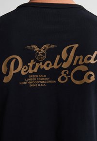 Zwarte katoenen t-shirt met gouden letters. De tekst omvat "Petrol Ind & Co" en "Green Gold Lumber Company, Northwood Wisconsin."