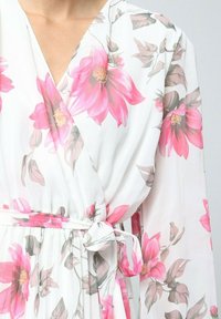 Robe portefeuille florale avec de grandes fleurs roses sur un fond blanc, à manches longues et avec un nœud décoratif à la taille. Tissu doux et léger.