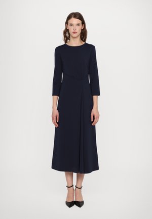 Navy blue midi dress, made of smooth fabric. Features a round neckline, three-quarter sleeves, and a pleated skirt. Black pointed heels.