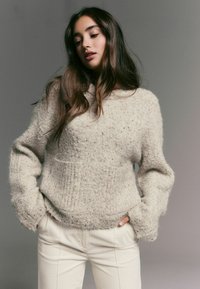 Bež kõrvarõngaga kudum, millel on tekstuurne pind, langevad õlad ja esikott, sobitub heledate pükstega. Pehme, paks kangas.