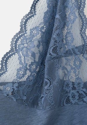 Tissu en dentelle bleue avec motifs floraux drapé sur un textile bleu lisse, montrant des bords festonnés et des détails délicats en filet.