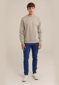 Beež vyššmiselge pehme kangaga, ümmarguse kaelusega, ribakäiste ja -servadega, koos siniste teksade ja valgete tossudega. Lihtne disain.