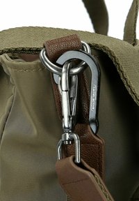 Oliven grøn nylon taske hjørne med et brunt læderhåndtag og en sølvmetal karabinclips fastgjort til en sikringssløjfe.