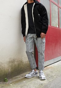 Černá kordurová bunda s bílou fleecovou podšívkou, ve spojení se šedými kostičkovanými cargo kalhotami. Obsahuje šedé běžecké boty New Balance. Hladká textura.