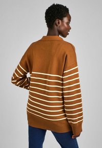 Pull en maille rayé marron avec un col et un ourlet côtelé. Arbore des rayures crémeuses horizontales sur le corps et les manches.
