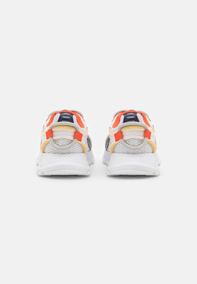 Zapatillas deportivas blancas con paneles de malla, acentos en naranja y amarillo, y suela acolchada. Presentan un talón prominente y un diseño flexible.