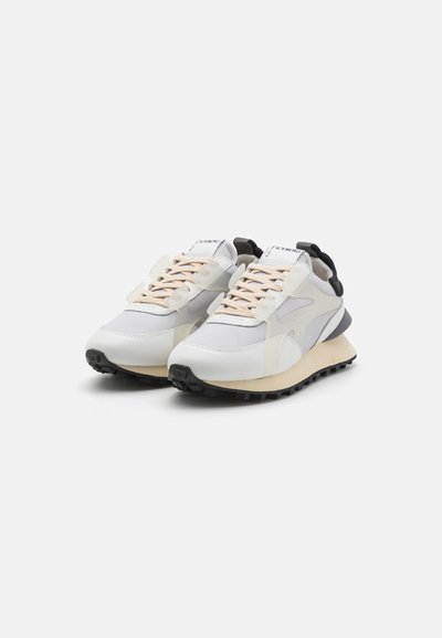 Sneakers with a mix of white and cream leather, black accents, and textured rubber soles. Features beige laces and a streamlined design.