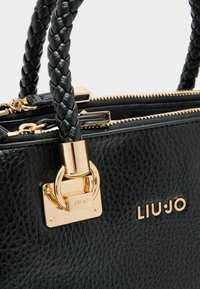 Sac à main noir texturé avec des poignées tressées, quincaillerie dorée et un fermoir rectangulaire. Présente le nom de la marque "LIU JO" en lettres dorées.