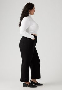 Black high-waisted pants with a straight leg, paired with a white ribbed turtleneck. Features a cropped fit and subtle hardware accents.