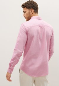 Camicia rosa a maniche lunghe con colletto, bottoni ai polsini e piega sul retro. Tessuto in cotone con una texture liscia e orlo curvo.