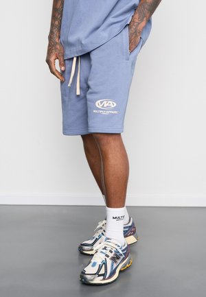 Light blue shorts with an elastic waistband and drawstring, featuring a white logo. Paired with white socks and multi-colored athletic shoes.