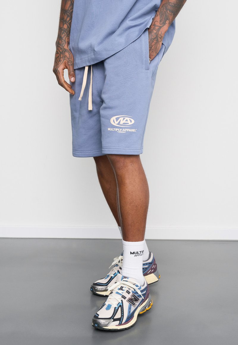 Light blue shorts with an elastic waistband and drawstring, featuring a white logo. Paired with white socks and multi-colored athletic shoes.