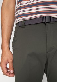 Mörkgröna byxor i lätt material, med en slät yta, två sidofickor och ett svart nätbälte.