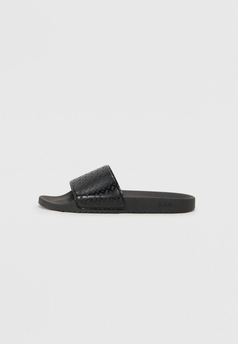 Sorte rutsjesandaler med en tekstureret, blank rem og en mat sål. Har en flad fodseng og et enkelt, åbent tådesign.