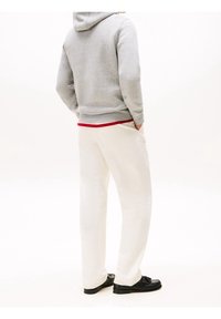 Sudadera con capucha gris, capa interior roja, pantalones blancos y zapatos negros. Los pantalones son holgados; la sudadera tiene un bolsillo tipo canguro y capucha con cordón.