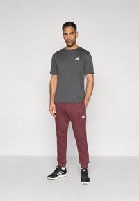 Γκρι κοντομάνικο μπλουζάκι με λευκό λογότυπο, συνδυασμένο με μπορντό φόρμες τζόγκερ με λευκό λογότυπο και μαύρα αθλητικά παπούτσια.