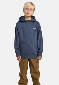 Tmavomodrá bavlnená mikina s kapucňou, s predným klokanie vreckom a rebrovanými manžetami, v kombinácii s béžovými cargo nohavicami.