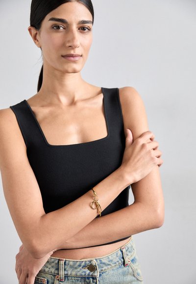 Μαύρο μπλουζάκι με τετράγωνη λαιμόκοψη και στενή εφαρμογή. Χρυσό βραχιολάκι αλυσίδας με κυκλικά στοιχεία. Ανοιχτό μπλε τζιν σορτς ψηλόμεσα με ξεθωριασμένη υφή.