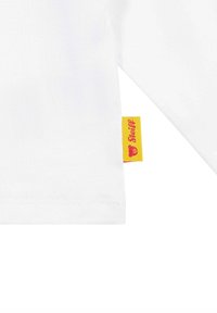 Weißes Langarmhemd aus weichem Baumwollmaterial. Besitzt ein gelbes Etikett mit roter Schrift am Saum, welches die Marke angibt. Keine Muster oder Grafiken.