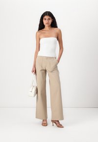 Beige videbukser med to frontlommer, sammen med en tettsittende hvit tube topp og beige stroppete hæl sandaler, mens hun holder en hvit veske.