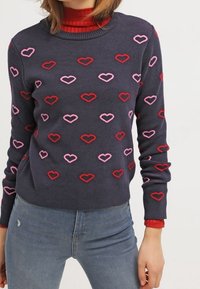 Maglione blu navy con motivi di cuori rossi e rosa, colletto e polsini a costine, realizzato in tessuto morbido, abbinato a un dolcevita rosso sotto.
