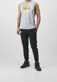 Szara koszulka bez rękawów z logo "Los Angeles Lakers", w połączeniu z czarnymi joggerami z purpurowymi akcentami i logo. Czarne sneakersy typu high-top.