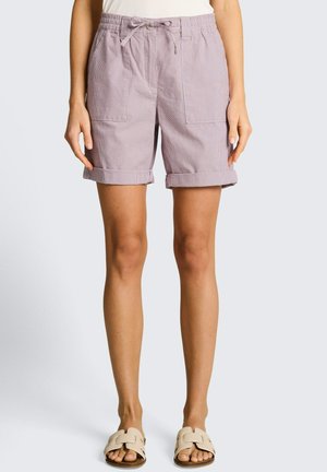 Lawendowe szorty z podwiniętymi mankietami, przednimi kieszeniami naszywanymi i ściągaczem w talii, noszone z beżowymi sandałami typu slide.