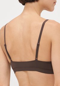 Smeđa bralette sa podešavanim trakama i glatkim, bešavnim pojasom. Karakterizira ga minimalistički dizajn bez vidljivih hardverskih elemenata ili ukrasa.