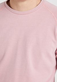 Felpa rosa chiaro con collo rotondo, maniche raglan e un tessuto liscio leggermente strutturato. Nessun motivo o accentuazione visibile.