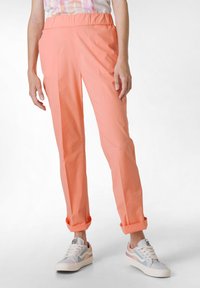 Pantaloni leggeri color corallo con una vita elastica, caratterizzati da un design a gamba dritta e orli arrotolati, indossati con scarpe da ginnastica multicolori.