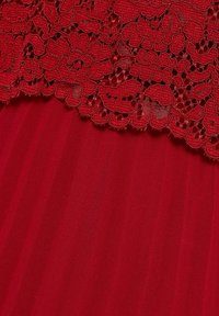 Tissu rouge avec une superposition de dentelle florale complexe et des bords festonnés au-dessus d’un matériau rouge uni et lisse.