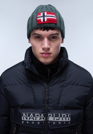 Bonnet tricoté vert avec une patch du drapeau norvégien rouge et blanc, porté par un mannequin dans une doudoune noire avec un logo en relief.