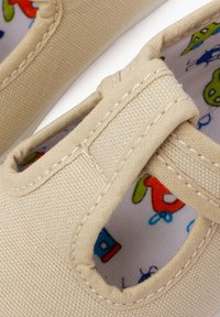 Beige plátěné boty se šitým vzorem a kulatými výřezy. Uvnitř mají barevný vzor s kreslenými postavičkami.