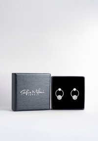 Silverfärgade hoopörhängen med en texturerad design, som har en central ädelsten och en klunga av mindre klara stenar, presenteras i en svart låda.