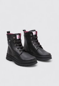 Une paire de bottines noires en cuir avec doublure intérieure rose, fermeture éclair sur le côté et lacets noirs avec des éclaboussures blanches sur un fond neutre.