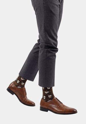 Braune Lederschuhe und dunkelgraue Hose kombiniert mit braunen Socken, die Kaffetassen, Becher und Desserts zeigen.